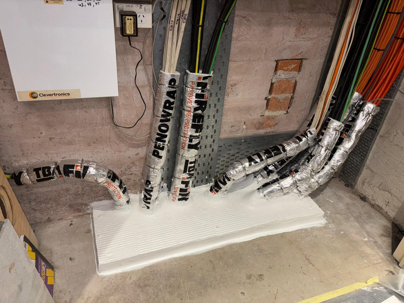 Cable bundles through a fire-rated wall sealed with Penowrap and TBA Firefly coated batts in a Sydney commercial fitout