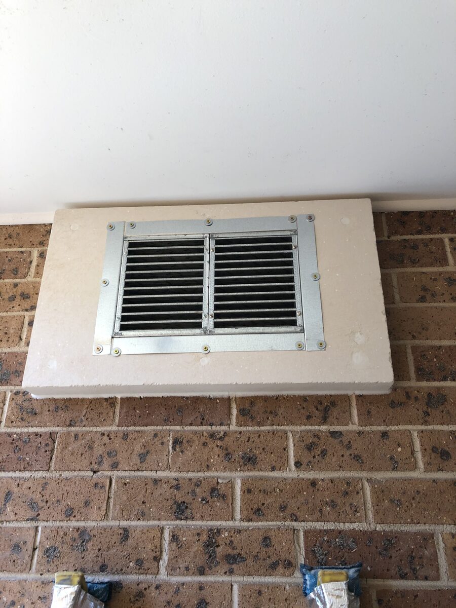 Intumescent fire damper louvre vent installed in a fire-rated wall opening on a brick wall